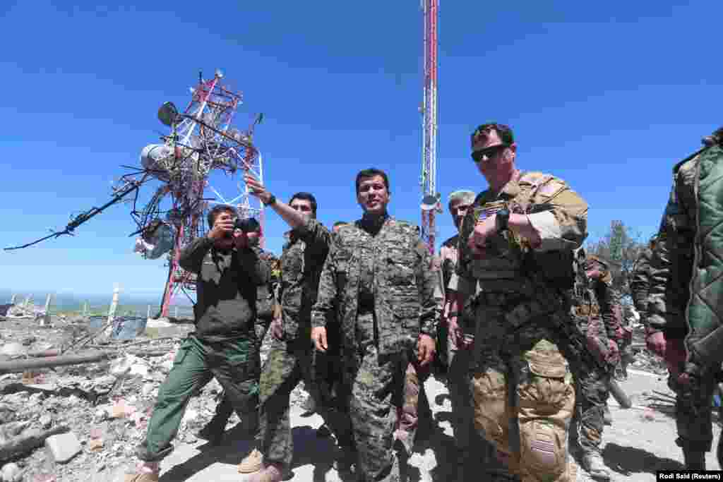 A U.S. military commander (right) with YPG fighters as they inspect the damage done to a YPG base after it was hit by Turkish air strikes. 