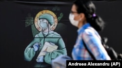 A woman walks by a depiction of medical staff wearing protective equipment, executed in the style of an Orthodox icon in Bucharest, Romania, on April 29.