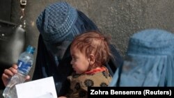 A displaced Afghan woman holds her child as she waits to receive aid supplies outside a UNCHR distribution center on the outskirts of Kabul.