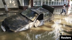 A local resident passes by a damaged car stuck in a flooded street in the town of Krymsk in Russia's Krasnodar region.